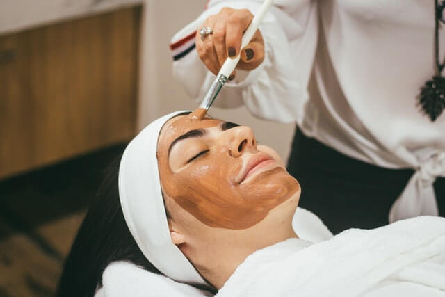 A Beauty salon appointment software user beautician is apllying face mask to her customer. 