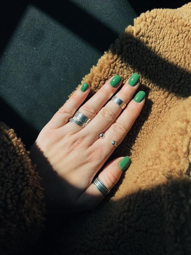 A Salon booking system user woman's hand with green nail polish.