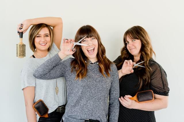 Three Beauty Software user hairdresser women are holding scissors and posing to the camera with a big smile.